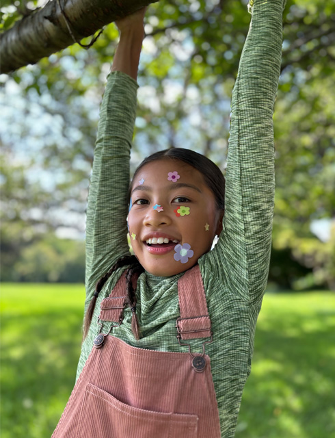 Fotografija djevojke u krupnom planu s naljepnicama u obliku cvijeća na licu snimljena s 2x telefoto zumom optičke kvalitete na iPhoneu 15